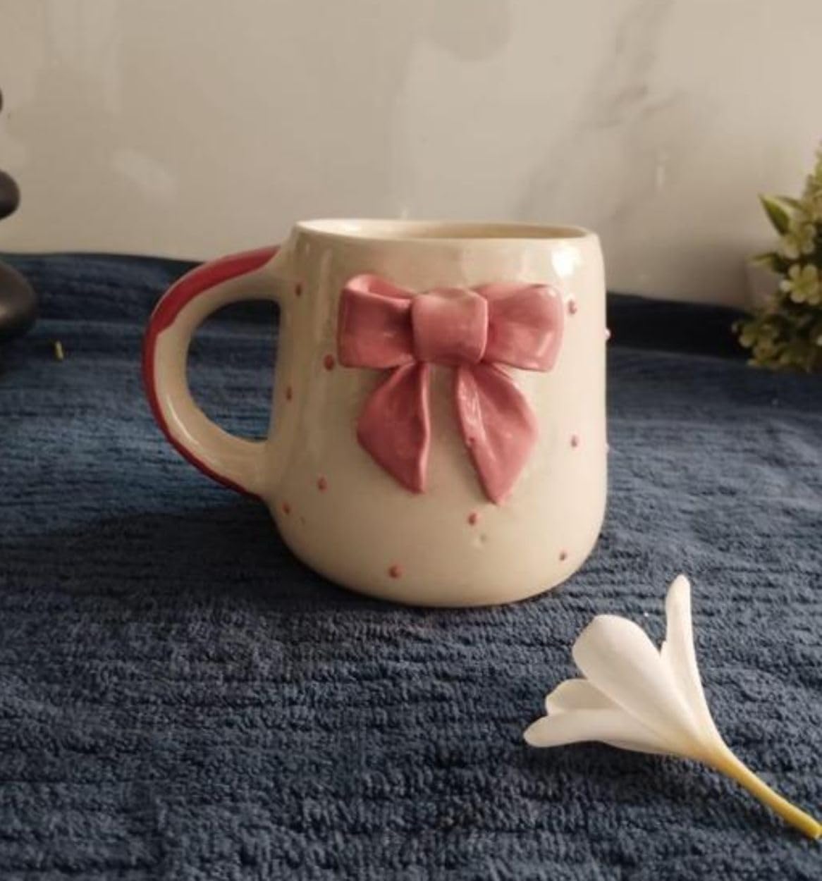 Cute handmade ceramic bow coffee cup on soft blue cloth background